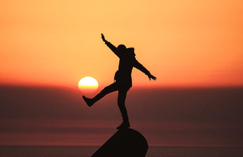 Man balancing on rock at sunset