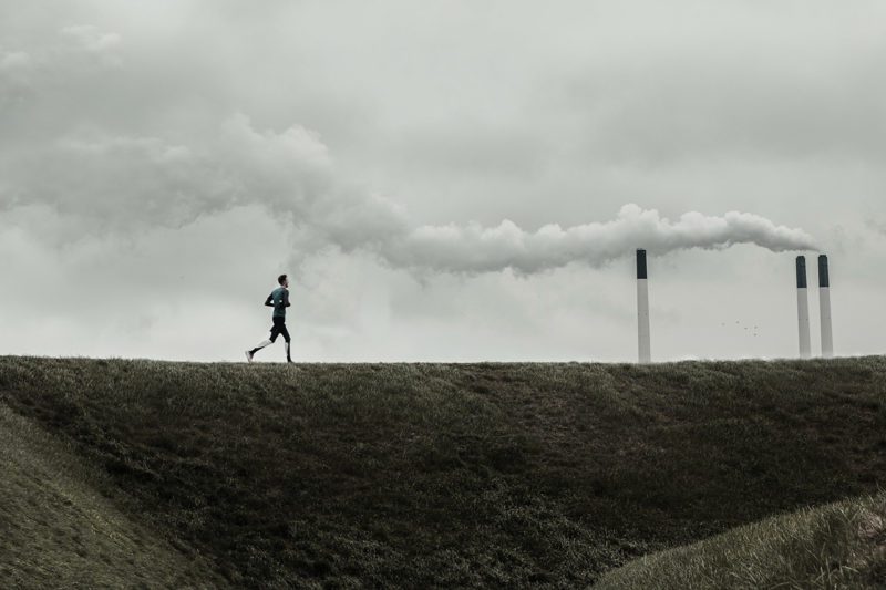 Man running next to smokestacks releasing pollution