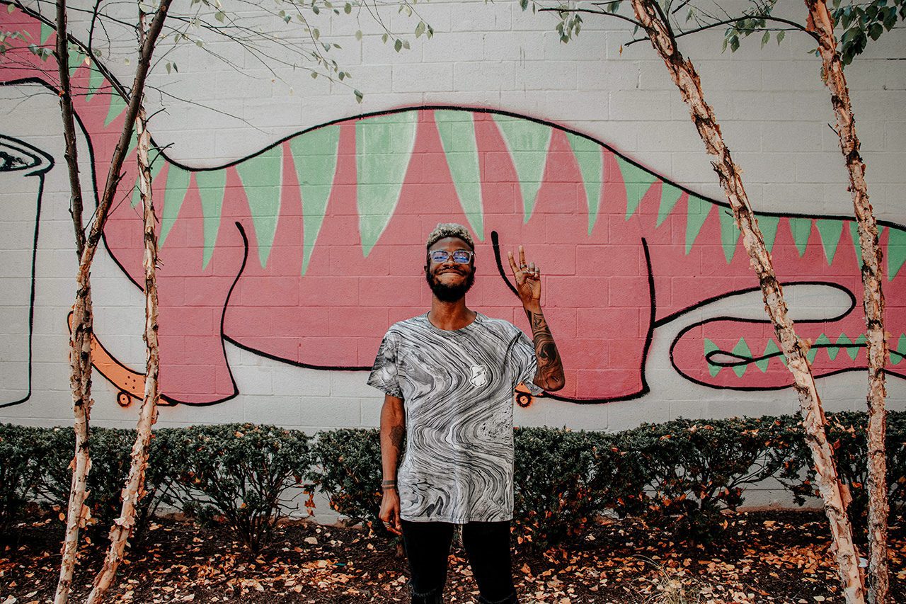 Black man in front of dinosaur mural