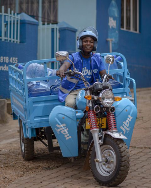 African man on motor bike pulling cart of Jibu water containers