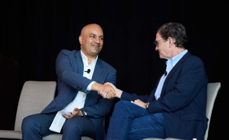 Two men on stage at conference shaking hands.