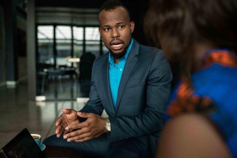Two businesspeople in conversation across a table as one gestures while discussing an investment or business strategy.