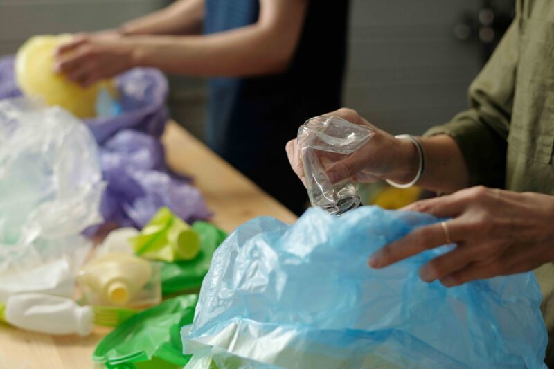 Close-up of hands sorting plastic bottles and packaging into bags on a table.