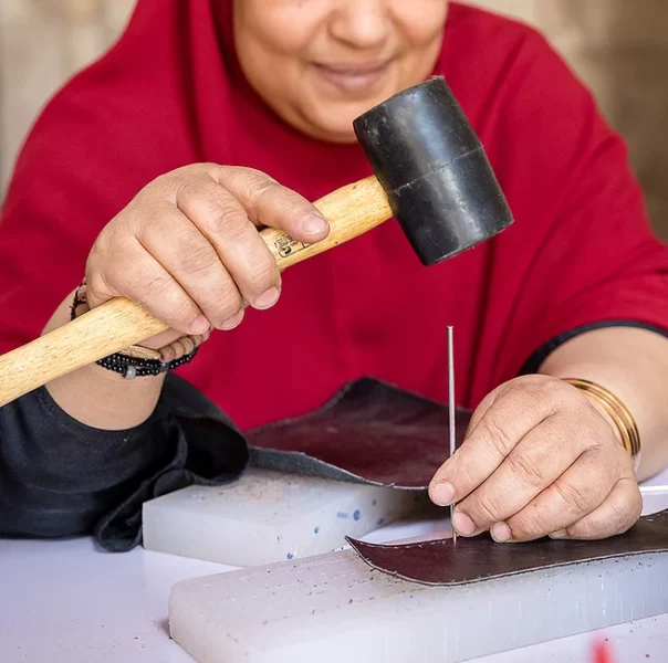A Mishkā artisan uses a mallet and hand tool to work a piece of leather.