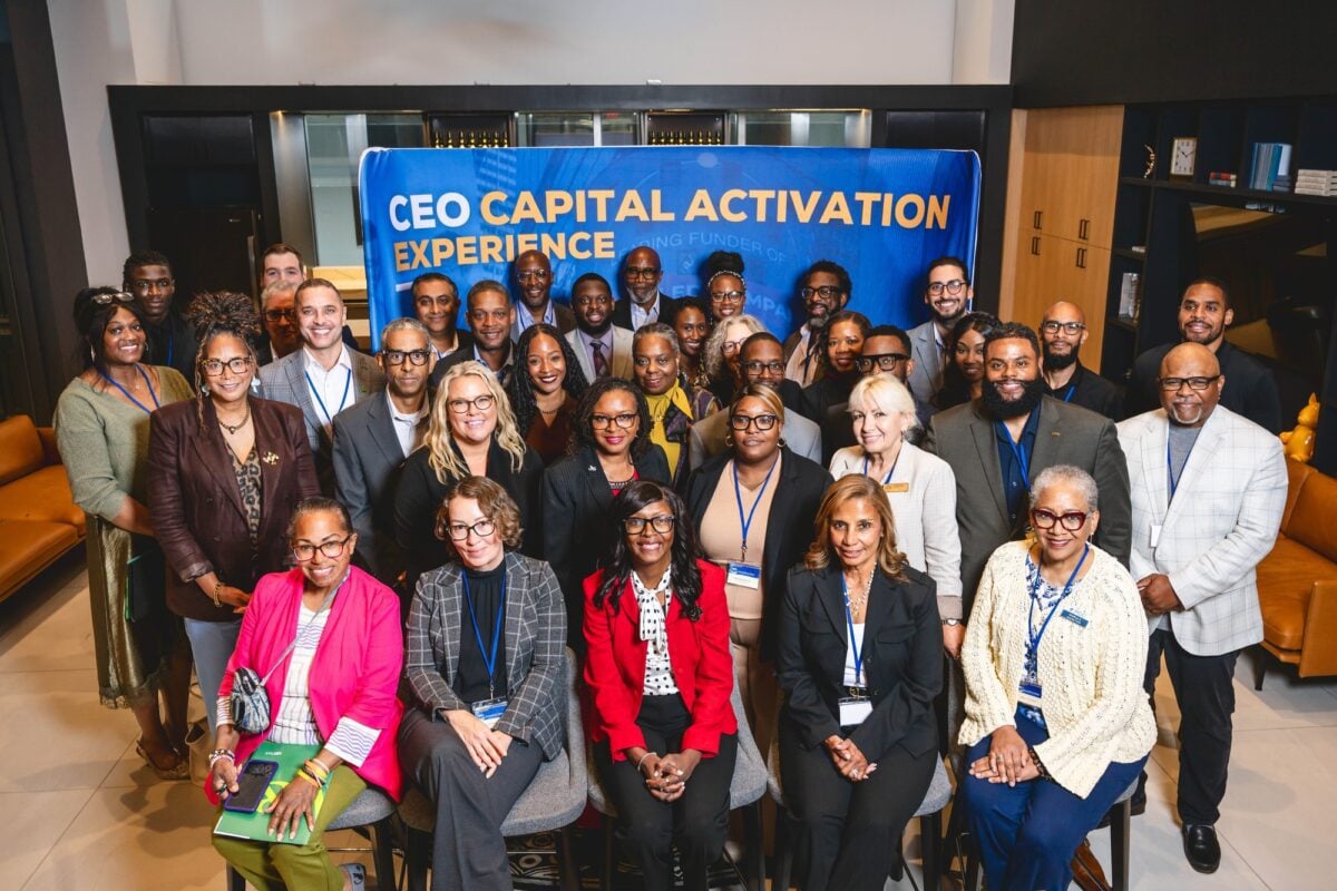 Several dozen people, many wearing name badges, pose in rows before a blue banner reading “CEO Capital Activation Experience”