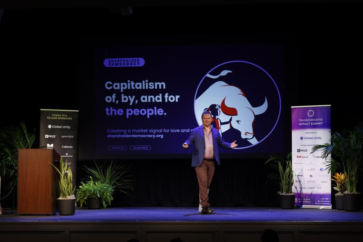 Gabriel Grant onstage beside a screen reading “Capitalism of, by, and for the people” at the Transformative Impact Summit.