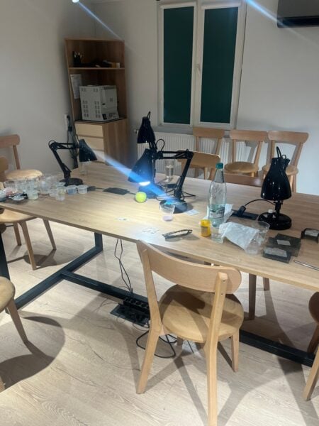 A jewelry-making worktable at Ikorta with adjustable lamps, small cups of materials, tools, and wooden chairs.