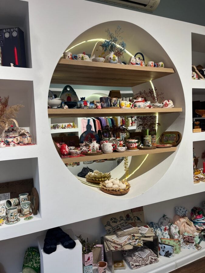 Painted ceramic cups and teapots, wooden items, and textiles arranged in a circular shelving display at ESKI.